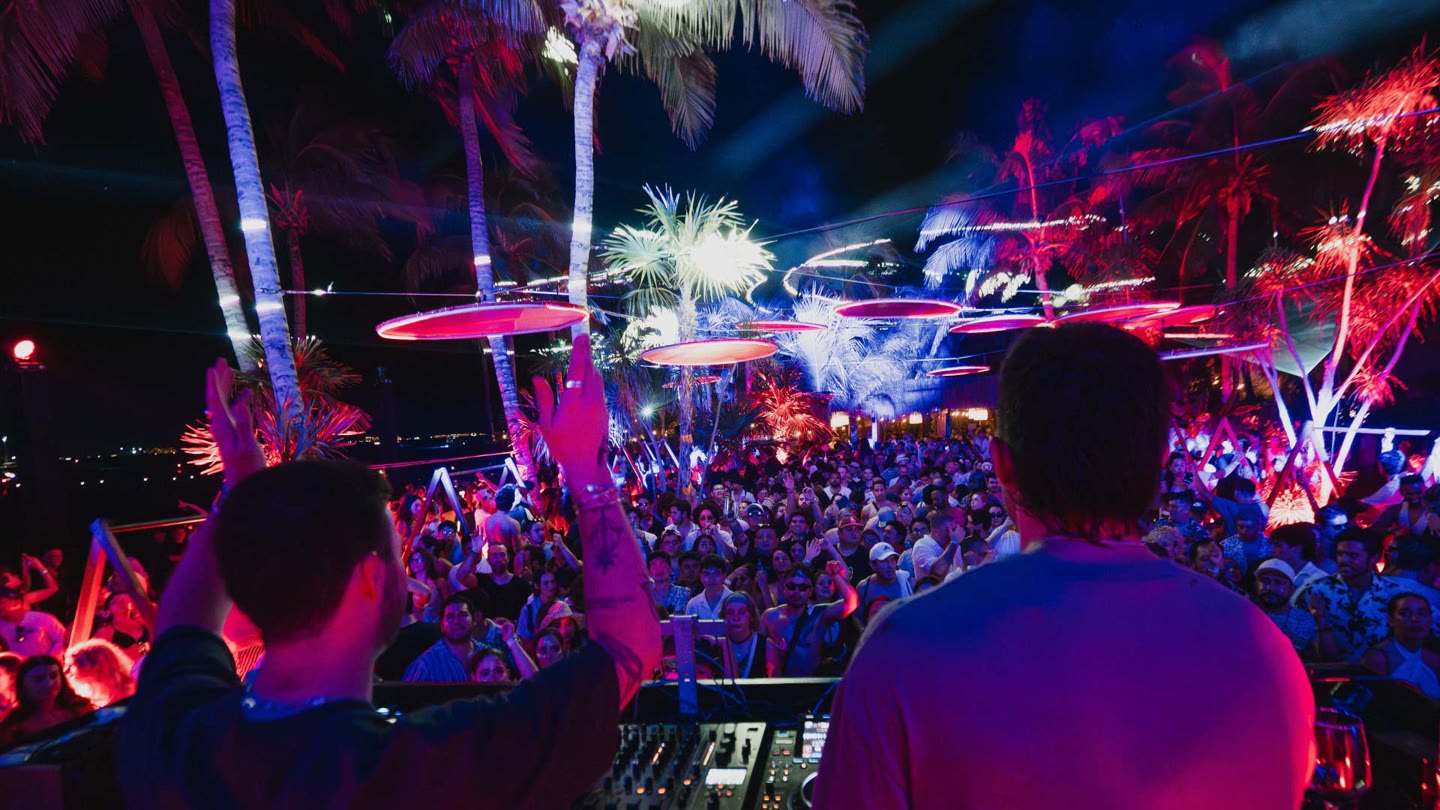 El público bajo las palmeras y las luces de neón en Terms & Conditions 2025, visto desde la cabina del DJ en Mayan Monkey Isla Mujeres